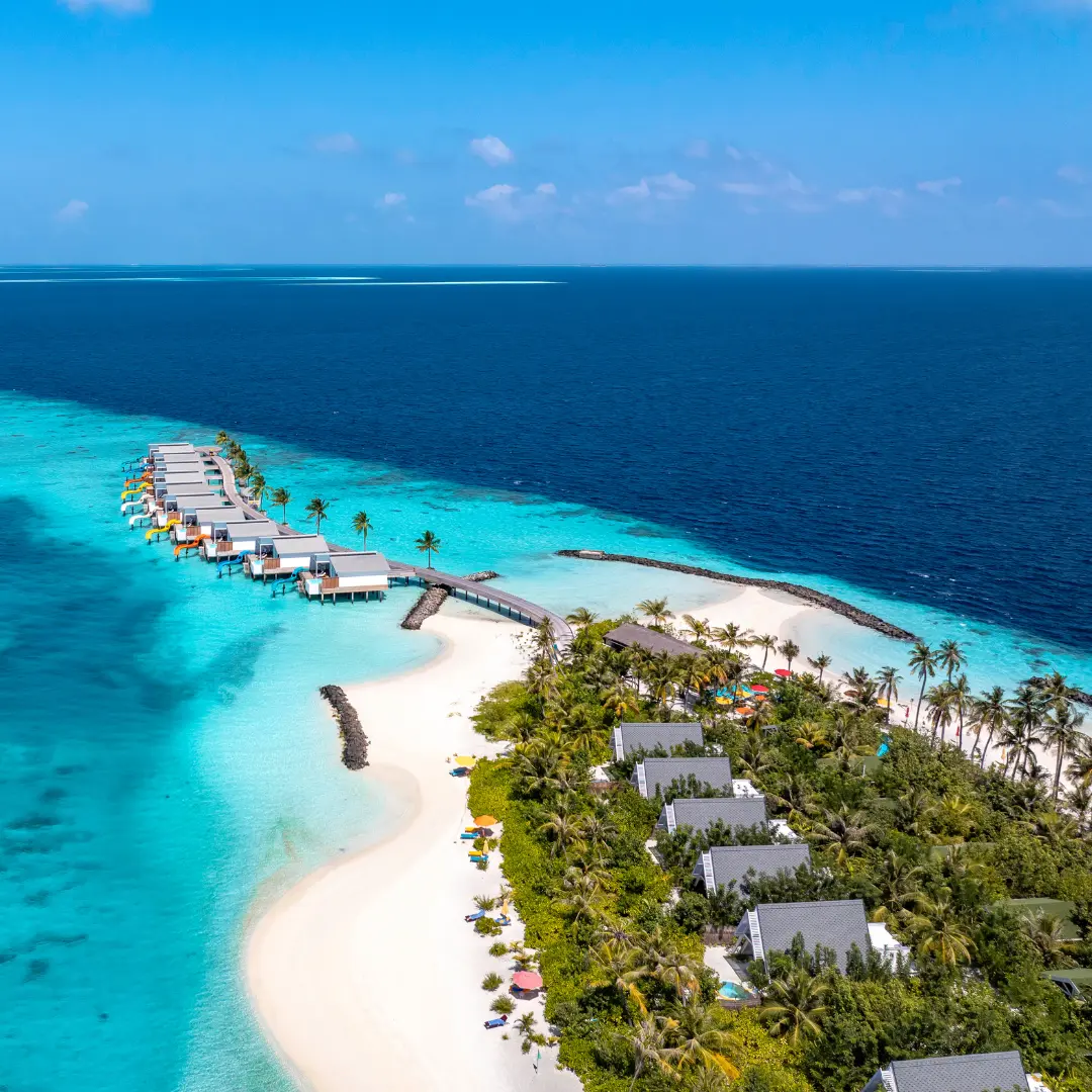 Aerial view of a Maldivian island fringed by overwater villas and turquoise reef